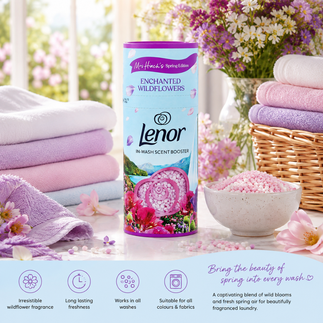Lenor Enchanted Wildflowers In-Wash Scent Booster bottle centered on a styled spring-themed set with folded lavender towels, a bowl of pink fragrance beads, flowers, and a basket of towels. A product info banner appears along the bottom.