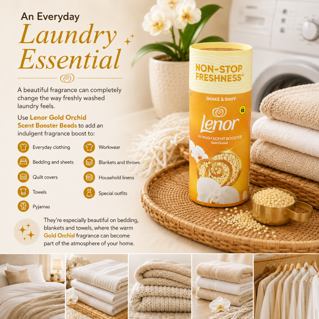 Lenor Gold Orchid Scent Booster Beads in a yellow and gold cylindrical tin, styled on a woven tray with folded beige towels and a small bowl of loose beads. The background is a warm, softly blurred laundry room scene with a washing machine and floral arrangement.